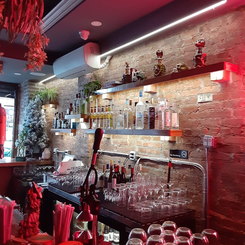 A dimly lit bar with red lighting, liquor bottles on shelves, and an array of glasses.
