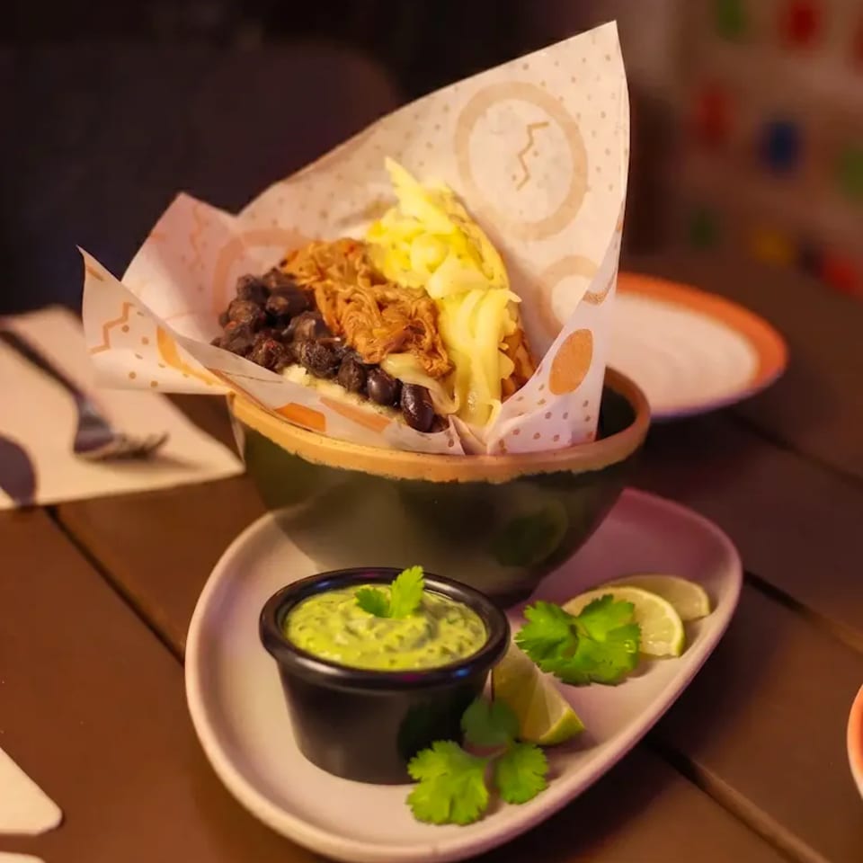 Arepa with black beans, shredded meat, and cabbage, served with green sauce and lime.