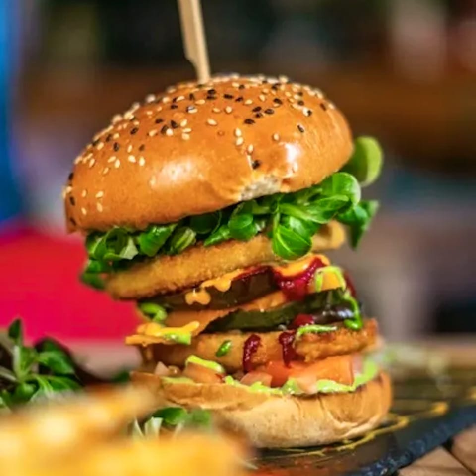 Tall, stacked burger with multiple patties, fresh greens, and sauces, served with fries.